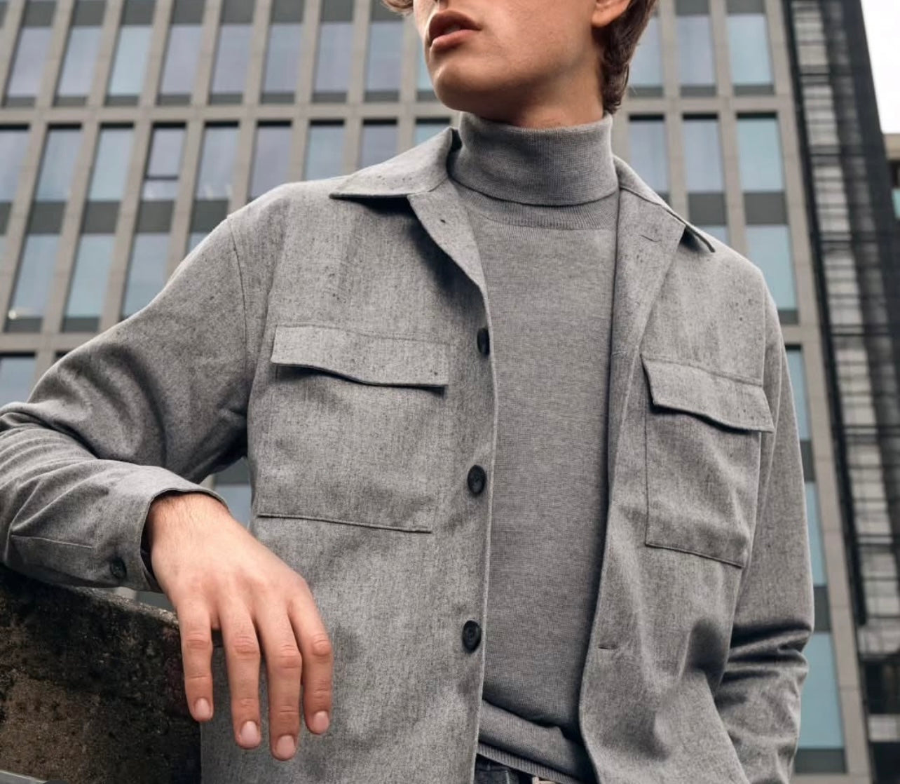 Person wearing a gray jacket and turtleneck in an urban setting