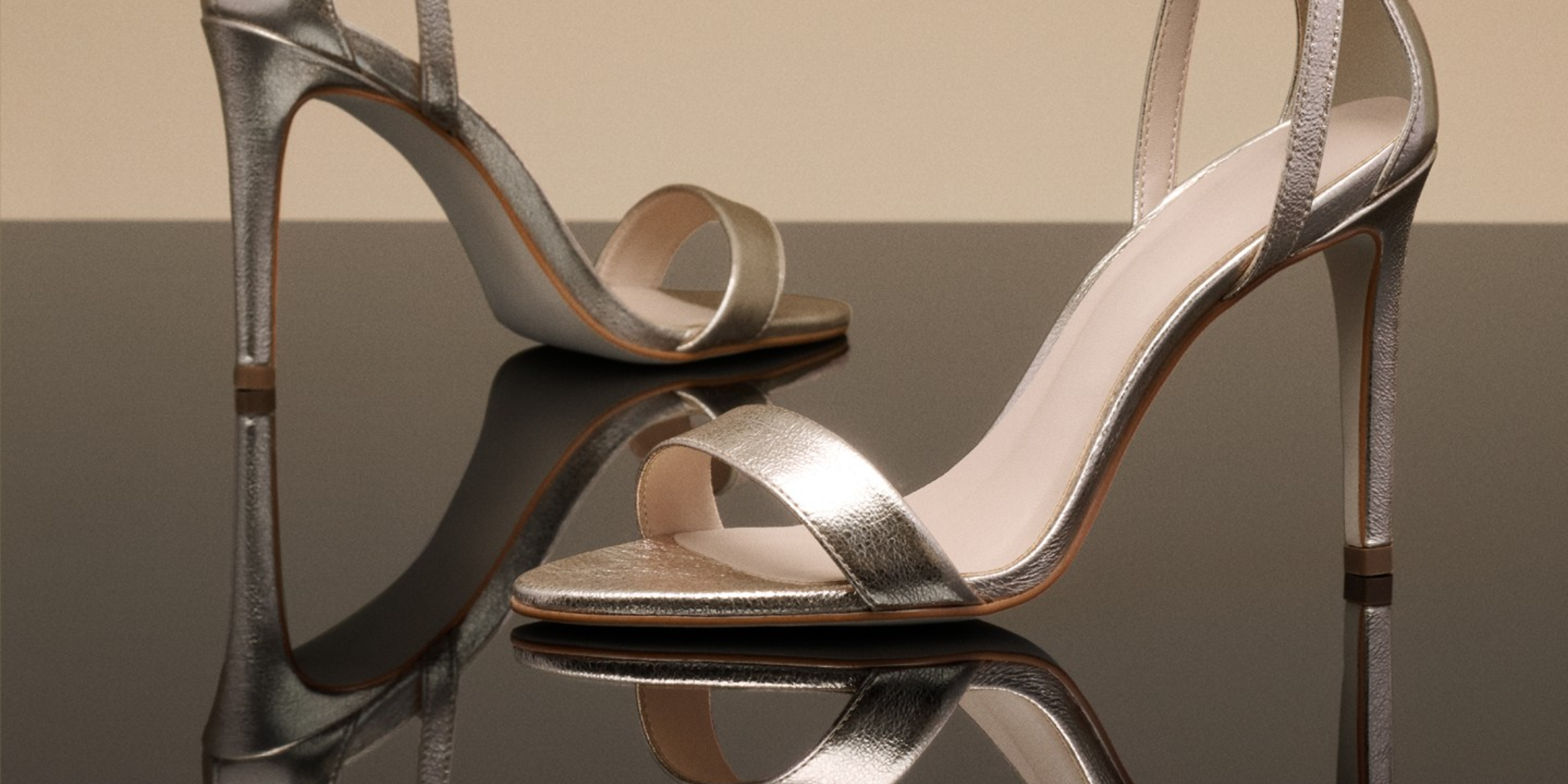 Silver high-heeled sandals on a reflective surface with a neutral background